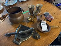 Overview of copper pot, pewter cups, copper skillet, small lidded pot, and other metal items on wooden table