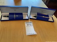 Two Waterman pens in original blue boxes with white interiors and accompanying Waterman brochures displayed on a wooden table.
