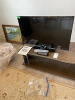 Full view of RCA 32 inch TV on stand with two remotes and manual nearby.
