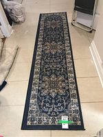 Long narrow blue floral runner rug laid out on a tile floor with intricate floral designs and patterned borders.