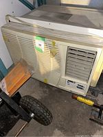 Front-side view of the window air conditioning unit showing vents, control dials, power cord, and some tape residue.