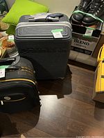 Front view of the gray Calvin Klein hard-shell suitcase with embossed logo, telescoping handle extended, positioned on wooden floor next to other bags.