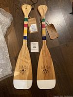 Two wooden paddles with colorful striped handles and white tips, laid on wooden floor. Each paddle is marked with Canada 150 commemorative engraving.