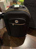 Front view of black carry on suitcase with yellow zipper and circular logo patch on pocket.