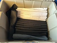 Folded chef aprons stacked in a large plastic storage bin, showing black, white, and striped aprons.