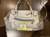 Front view of the light grey leather Coach bag showing dual handles, front zip pocket with gold-tone hardware, and shoulder strap.