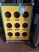 Front view of the vintage cornhole board showing nine scored holes with various point values and yellow playing surface with green frame.