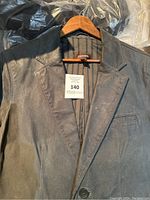 Front view of Danier men’s gray nubuck leather jacket hung on a wooden hanger, showing the smooth texture and front button closure.