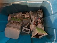 Wide view of a bin containing assorted electrical outlet and switch covers, switches, and unknown small components.