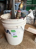 White bucket with various metal gas fitting tools visible inside, including pipe wrenches and a brass pressure gauge with large dial.