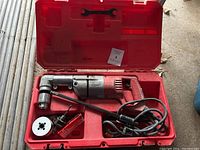 Complete Milwaukee hammer drill kit shown in red carrying case including drill, handle, accessories, and documentation.