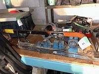 Side view of a manual metal tube bender showing the orange and black handle, blue metal clamp, and the label plate.