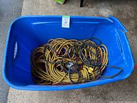 Blue plastic tub containing coiled heavy duty extension cords, mostly yellow with black stripes and one solid black cord.