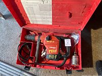 Red Hilti rotary hammer drill in molded plastic case with side handle, cord, SDS Max bits and paperwork