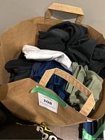 Paper bag filled with assorted men's active wear tops in various colors.