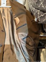 Photo of the inside of a brown men's cashmere coat showing beige satin lining and interior zipped pocket with 'Burberry' label sewn inside.