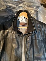 Close-up image of Danier brand label inside collar of black leather jacket on hanger showing collar and upper front part of jacket.