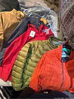 Photo of 5 men's jackets laid out on a surface showing different colors and styles including tan, dark blue, red, green, and orange jackets.