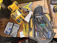 Top view showing yellow drill bit cases, tool bag filled with screwdrivers and miscellaneous tools on wooden surface.
