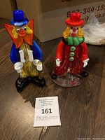 Photo showing two Murano glass clown figurines side by side on a floor with auction tag in front.