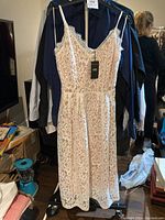 Full view of white lace dress on hanger showing its length and shape with new tags attached.