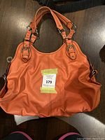 Front view of orange Nine West handbag showing dual handles and silver-tone buckles on a dark surface.