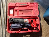 Milwaukee reciprocating saw with power cord inside a red plastic carrying case.