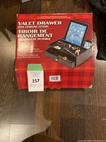 Boxed valet drawer with charging station, shown on floor, front of box visible with product details and images.