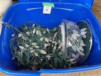 Two reels of white LED Christmas light strings with green wiring and textured pine cone shaped bulbs inside a blue plastic bin