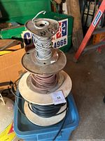 Four large and small spools of electrical wires stacked in a plastic bin, showing gray, red and black wires.