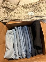 Box of various folded women's jeans in shades of blue, black, and snake print visible on top.