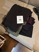 Stack of six pairs of women's workout pants folded on a couch showing various dark colors including black, olive green, dark purple, and navy.