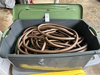 Top view of two coiled garden hoses placed inside a large grey plastic tote with an olive green lid set beside it.