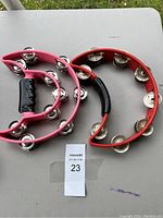 Both tambourines lying flat on a table side by side, showing full view of pink and red tambourines with metal jingles and black handles.