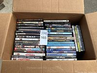 Overhead view of cardboard box packed with about 75 DVDs. Titles visible include Monsters Ball, S.W.A.T., Dejavu, Duplicity, and more.