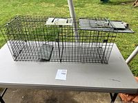 Front and top view of the rectangular wire mesh live animal trap showing spring-loaded door and handle.