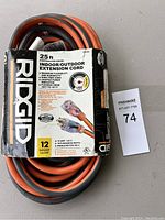 23ft orange extension cord coiled with RIDGID branded packaging attached, showing detailed product info and usage