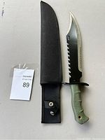 Knife placed next to black sheath on a gray surface with auction tag showing number 89.
