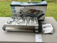 Buffet server with three compartments and clear lids along with original box and manual on a table outdoors.