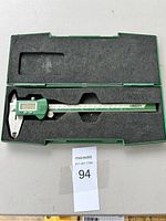 Full view of the digital caliper resting inside its green protective case with black foam.