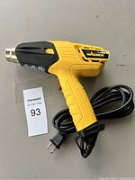 Side view of yellow Wagner heat tool with black grip and power cord coiled beside it on a gray surface.