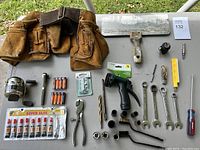 Full lot layout showing leather tool belt, hand drill, wrenches, sockets, pliers, drill bits, batteries, super glue, tile scraper, screwdriver, and utility blade.