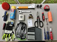 Photo of the tool lot showing various hand tools, gloves, drill bits, and accessories arranged on a table.