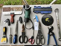 Top view showing various hand tools on a table including scrapers, screwdrivers, scissors, a saw blade, and a contour gauge.