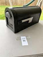 Black mailbox with U.S. Mail label visible, front flag, and placed on a table outdoors.