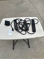 Four outlet strips placed on a white folding table, showing a small square adapter and three black rectangular power strips with power cords.