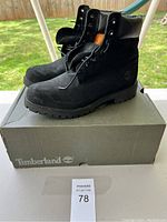 Side perspective of Timberland boots on the original branded box, showing exterior black leather and sole tread.
