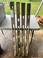 Four vintage wooden carpenter levels leaning against table on concrete floor, showing bubbles and cutouts.