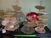 View of all tiered cake servers, pedestal plates, and red plastic plate on a black cart.