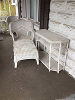 View of the white wicker chaise lounge and hall table placed on a porch with visible wear and tear.